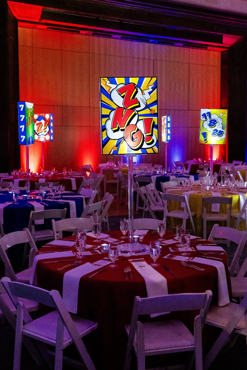 Custom comic-book illuminated centerpieces repeated throughout a colorful event dining room