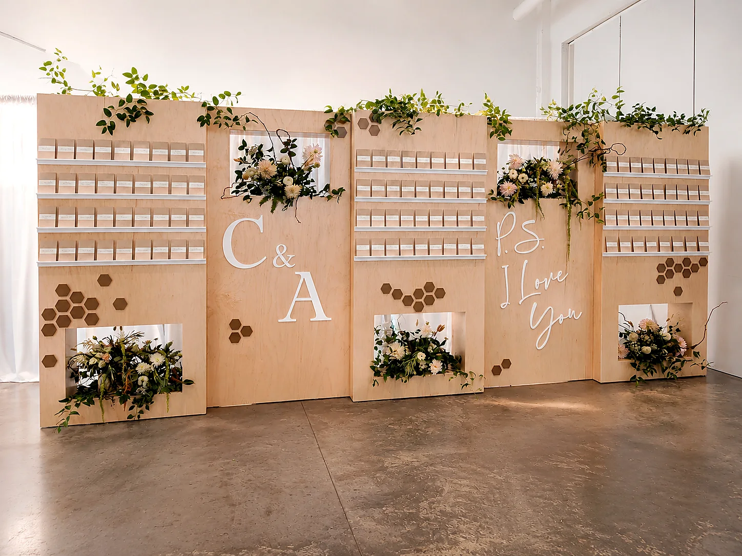 Custom natural wood wedding escort card wall with greenery, flowers and personalized lettering