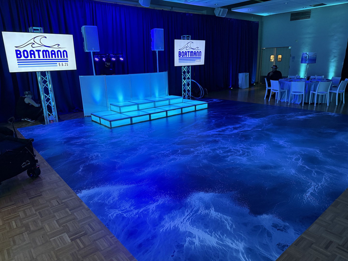 Ocean-themed custom floor wrap with an illuminated stage, DJ facade and blue event lighting