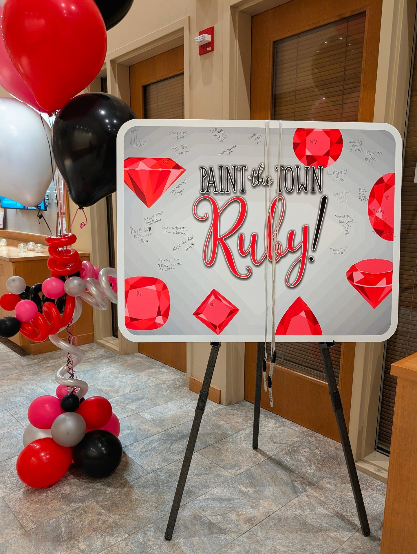 Ruby-themed custom sign-in board on an easel with red gemstone graphics and balloon decor